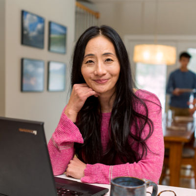middle-age woman at laptop, two teens in the background